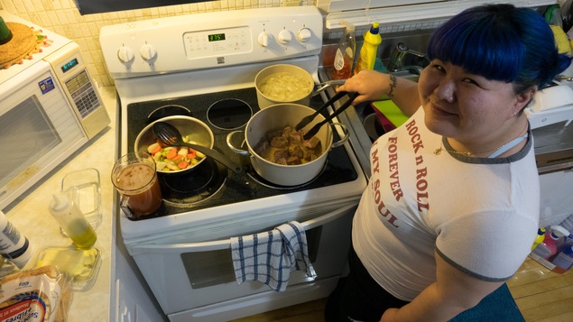 Une jeune femme pose dans une cuisine devant une cuisinière remplie de chaudrons en train de cuire.