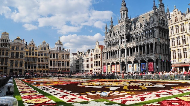 Un parterre fleuri en forme de motifs savamment exécuté occupe le centre de la place. Des bâtiments à l'architecture raffinée se dressent autour.