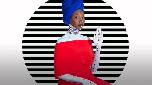 La chanteuse malienne Fatoumata Diawara prend la pose dans une robe rouge saillante devant un fond blanc ligné noir.