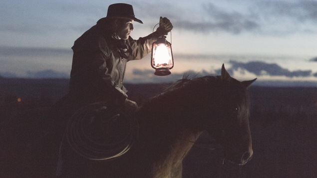 Un cowboy tient une lampe à l'huile en se baladant à cheval.