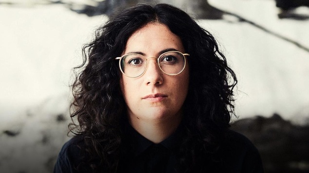 Alexandra Stréliski portant des lunettes et regardant directement la caméra, vêtu d'une chemise noire