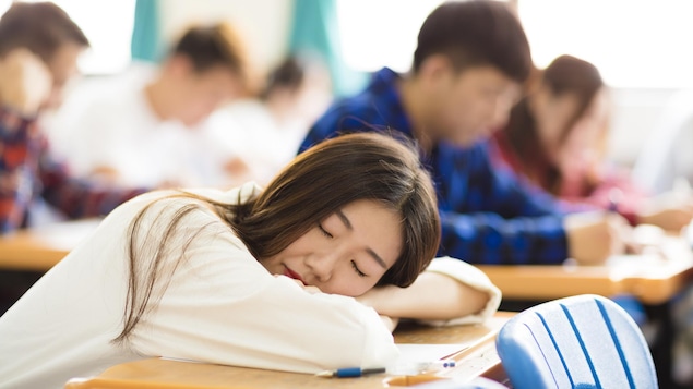 Une étudiante dort sur son pupitre pendant un cours.