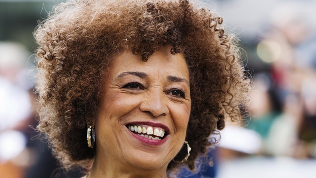 Elle a les cheveux bouclés et des boucles d'oreilles rondes.