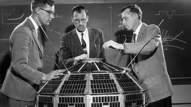 Trois scientifiques en veston observent et touchent au satellite Alouette 1, en 1961.