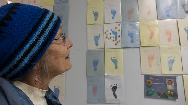 Une femme regarde un mur recouvert d'empreintes de pied de nouveaux nés.