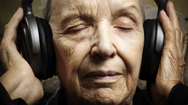 Une femme âgée écoute de la musique dans des écouteurs et son visage évoque le bien-être.