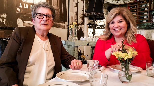 Les deux femmes posent assises à une table à la nappe blanche.