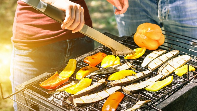 Une femme tourne des légumes avec une pince sur un BBQ.