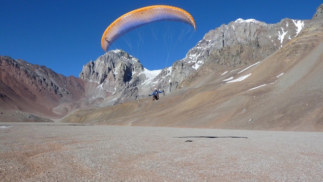 Un homme fait du parapente dans les montagnes avec du ciel bleu en arrière plan.