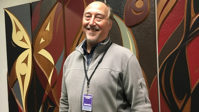 L'historien Maurice Guilbord pose pour une photo devant une oeuvre d'art dans les studios de Radio-Canada à Vancouver