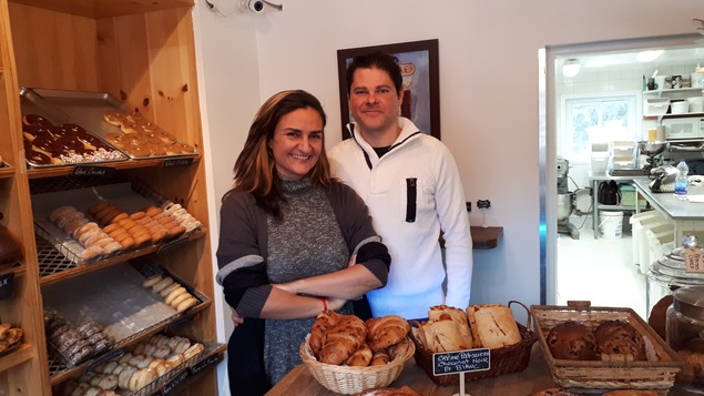 Soraya Zarate et Christian Denis, propriétaires de Beignes Dora, postés derrière le comptoir de leur boulangerie, rempli de pâtisseries.
