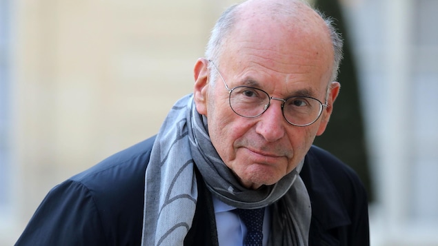 Un homme avec des lunettes et portant un foulard regarde la caméra.