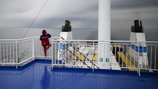 Vu de dos, un enfant se trouve sur le pont supérieur d'un cargo et regarde la mer.