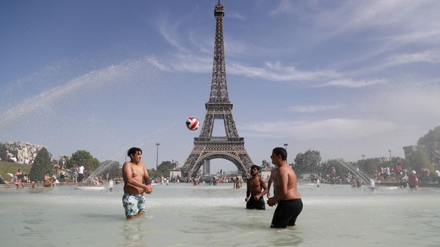 Des garçons joue au ballon dans une fontaine devant la tour Eiffel.
