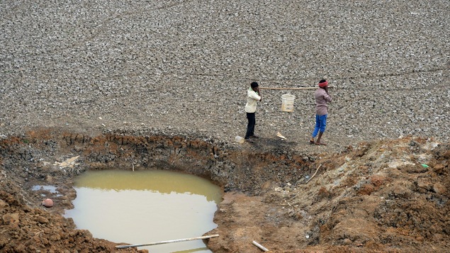Deux travailleurs indiens transportent un seau d'eau puisée à même un étang asséché.