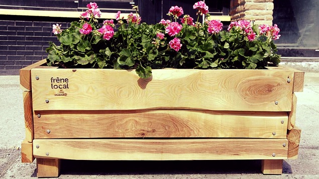 Un bac en bois avec des fleurs roses sur un trottoir.