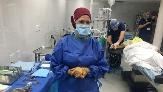 Une femme de l'équipe médicale pose pour la caméra pendant qu'un docteur s'occupe d'un patient.