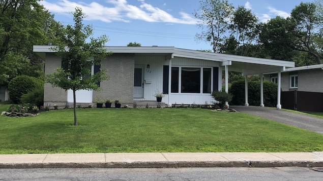Une maison à un étage faite de brique grise et de vinyle blanc avec une large fenêtre sur la façade et un abri d'auto sur le côté.