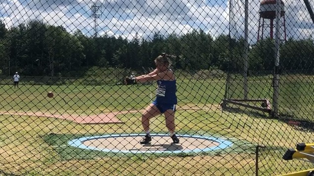 La jeune athlète Camille Desjardins en train de faire un lancer du marteau, sur un terrain dehors.