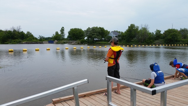 La photo présente trois enfants vêtus de vestes de flottaison qui pêchent sur un quai.