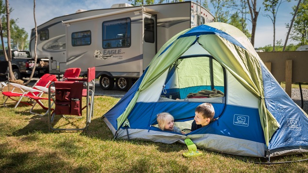 Roulotte et petite tente sur un terrain de camping gazoné avec des enfants