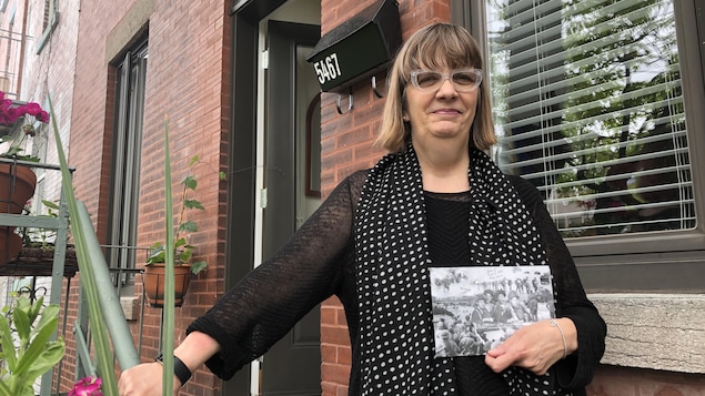 Une femme devant la porte d'entrée d'un appartement tenant une carte postale en noir et blanc.