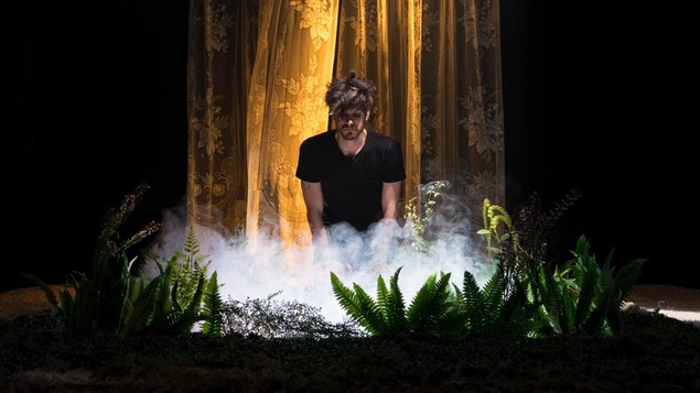 Un homme à genoux au milieu de la scène regarde de la fumée s'échapper d'un trou bordé de plantes.