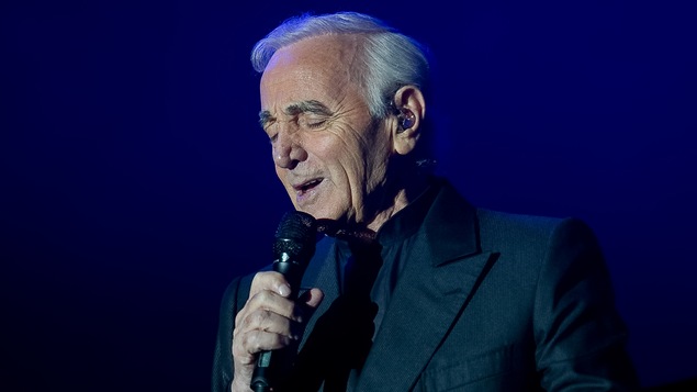 Charles Aznavour chante micro à la main, les yeux fermés.