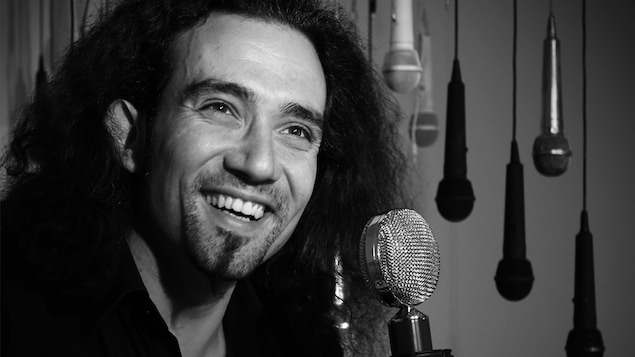 Le chanteur souriant Clément Courtois en gros plan devant un microphone avec en arrière plan des microphones suspendus du plafond.