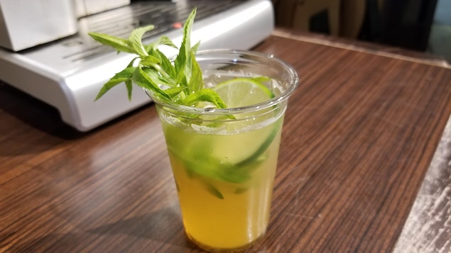 Gros plan d'un verre contenant un liquide doré avec une branche de menthe et une rondelle de lime.