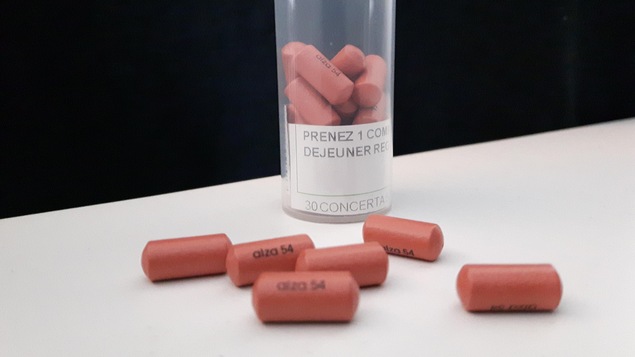 Un contenant en plastique et des comprimés de Concerta de 54 mg déposés sur une table blanche.