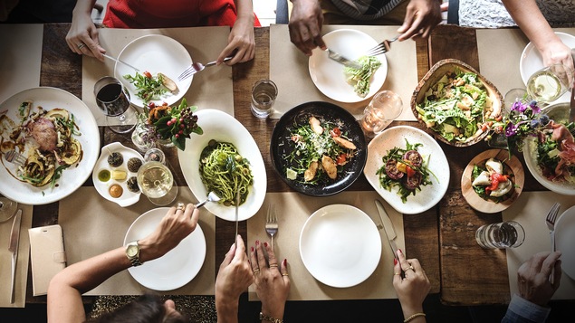 Il y a six personnes à table, ils mangent des champignons, des pâtes, de la salade et d'autres mets.
