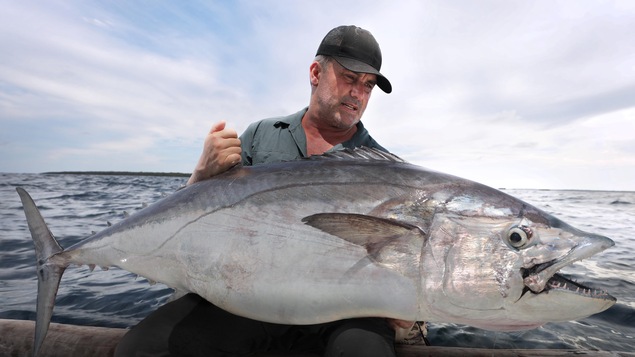 Un homme sur une embarcation tenant un gros poisson.
