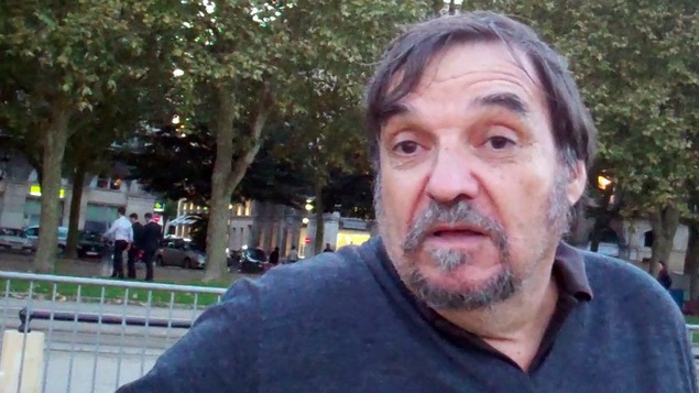 Un homme assis dans un parc parle à la caméra.
