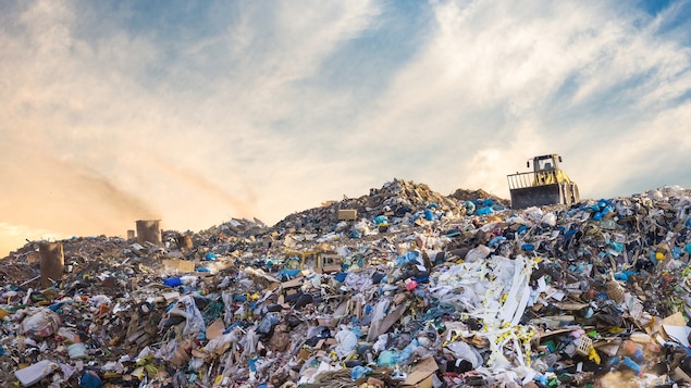 Un véhicule repousse des piles de déchets dans un dépotoir.