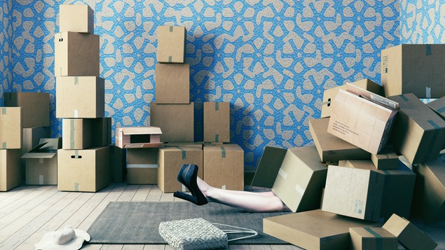 Les jambes d'une dame se dégagent sous une pile de boîtes, dans une maison en plein déménagement.