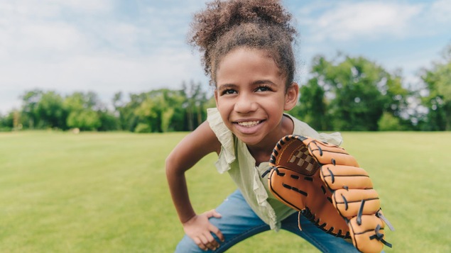 Une jeune fille afro-américaine, souriante, avec un gant de baseball dans un champ.