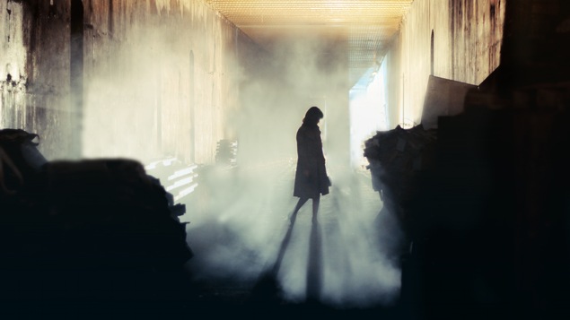 Une femme en manteau dans une rue sombre.