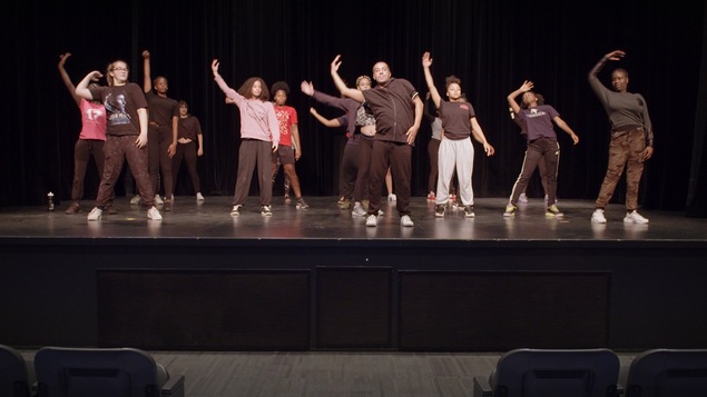 Des jeunes filles sur une scène en train de pratiquer des mouvements de danse avec leur chorégraphe