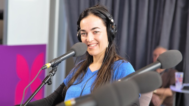 Émilie Monnet sourit, assise derrière un micro.