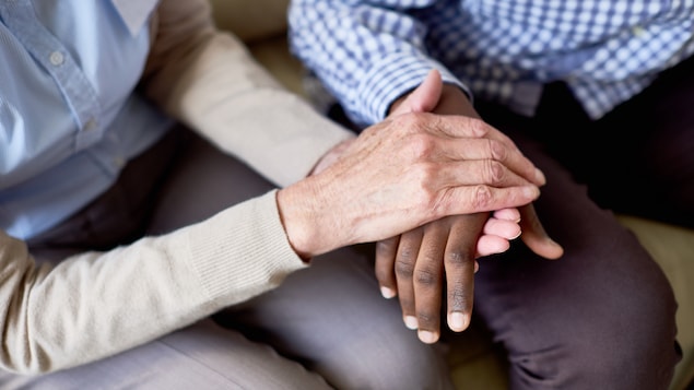 Les mains d'une personne d'un certain âge, offrant un support moral en tenant les mains d'un jeune, à la peau noire.