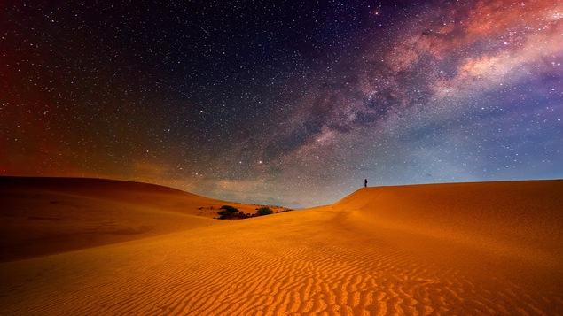 Une dune dans le désert sous un ciel étoilé rappelant l'espace.