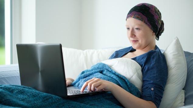 Une jeune femme atteinte du cancer regarde une vidéo sur un ordinateur dans son lit.