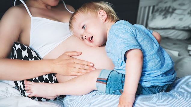 Un enfant penche sa tête sur le ventre de sa mère, qui est enceinte.