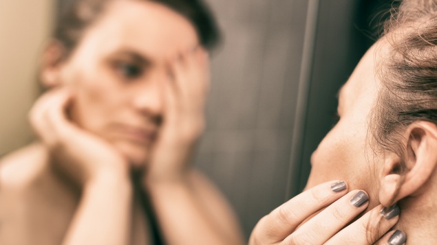 Une femme se trouve un défaut en se regardant dans le miroir.