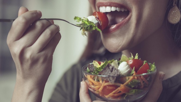 Une femme mange une salade.