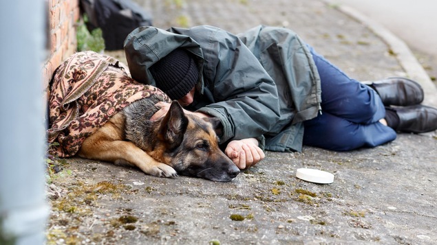 Un jeune itinérant dors sur le trottoir avec son chien.