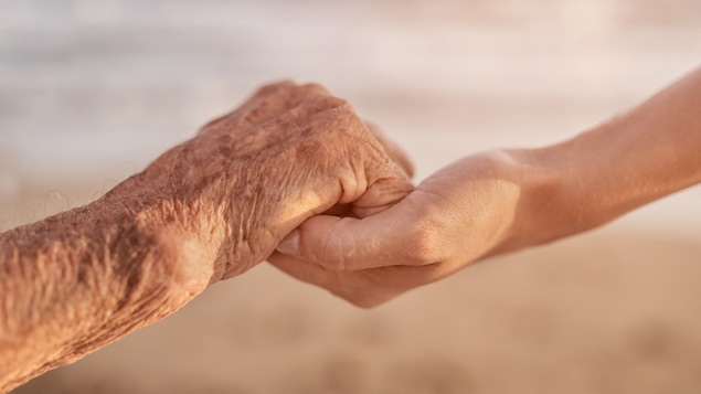 Une personne en fin de vie tient la main d'une autre personne.