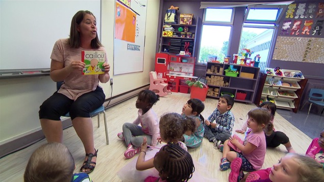Une enseignante lit un livre à des enfants assis devant elle.