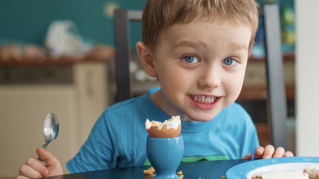 Souriant, un jeune garçon savoure une oeuf mollet dans sa coquille pour le déjeuner.